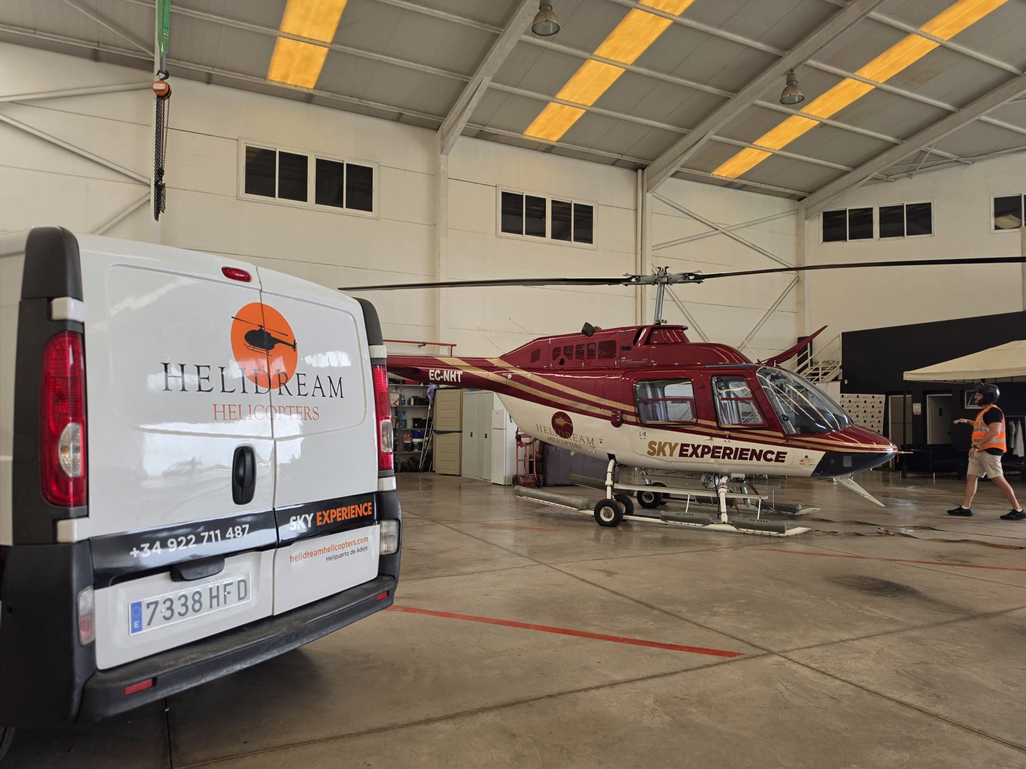 Furgoneta corporativa y helicóptero rotulados en el hangar del Helipuerto de Adeje
