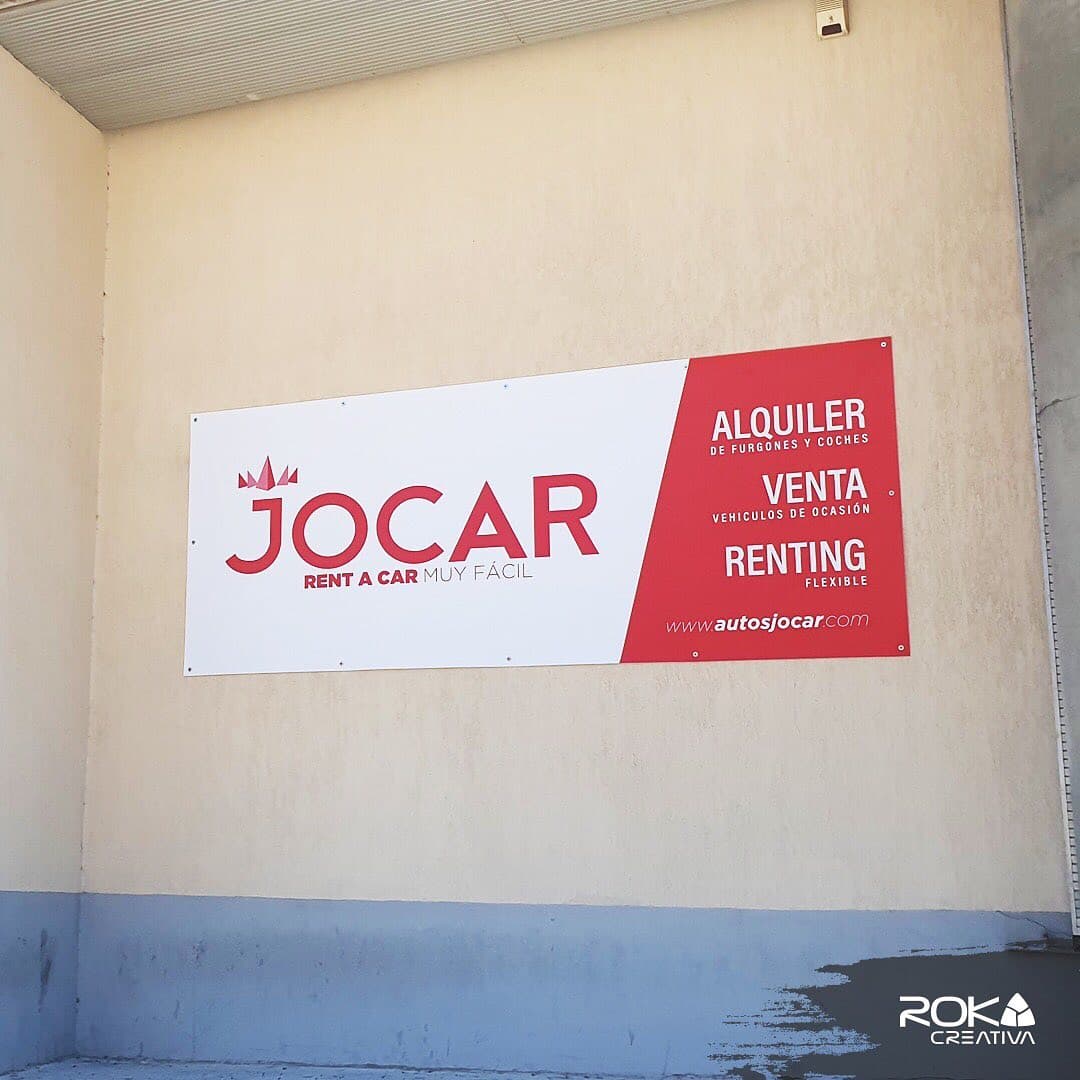 Lona publicitaria con ojales de Jocar Rent a Car instalada en la fachada